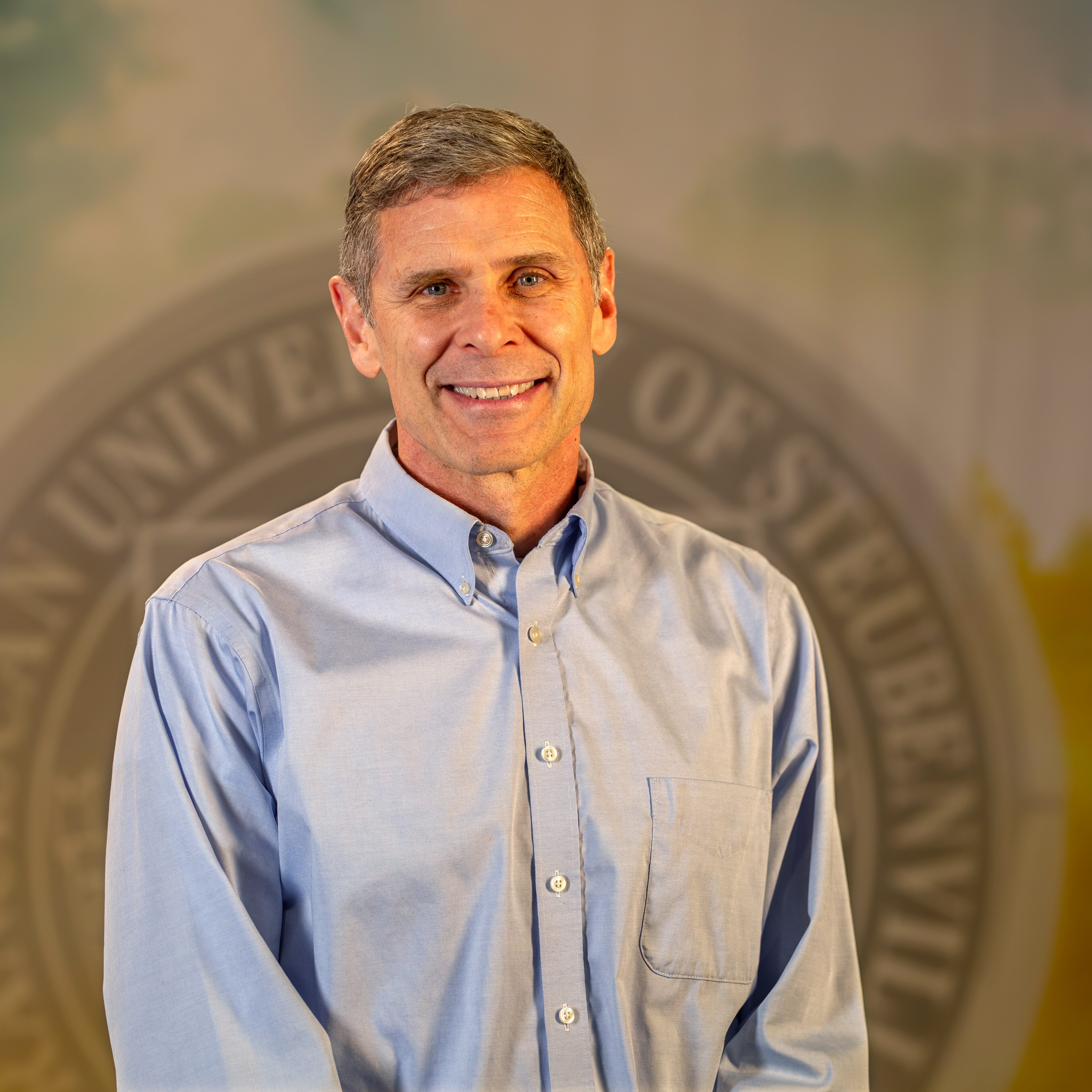 Dr. Jeffrey Rohde standing in front of university seal.