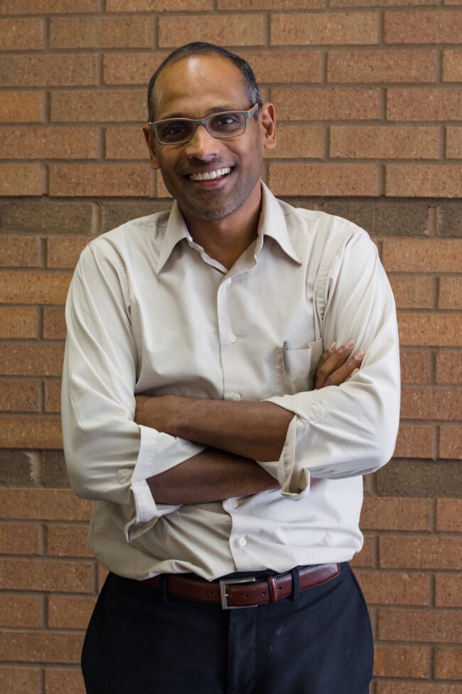 Portrait of Dr. Joseph Pathakamuri standing in front of a brick wall.
